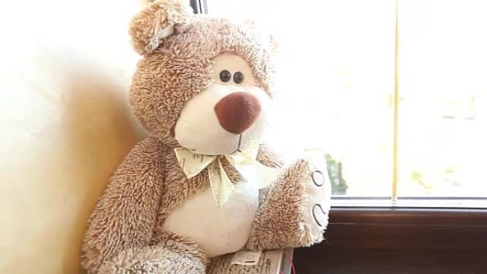 泰迪熊坐在窗台上，可爱的泰迪熊靠近窗户，脖子上有一只蝴蝶，浅棕色，儿童毛绒玩具，一只泰迪熊脖子上有一