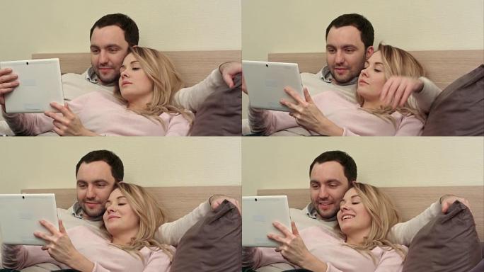 躺在床上的年轻夫妇使用平板电脑在互联网上购物