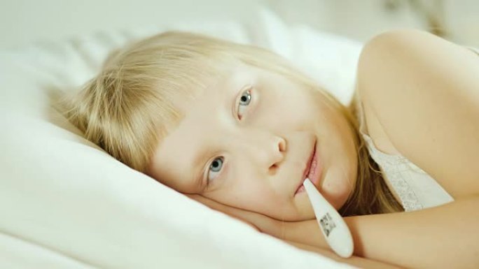 一个小女孩用电子温度计测量。孩子躺在床上。4k视频