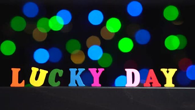 五彩缤纷的词汇 “幸运日” 来自抽象模糊灯光前的多色木制字母bokeh背景