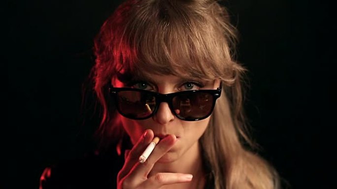 戴眼镜的金发女人在黑色背景上抽烟