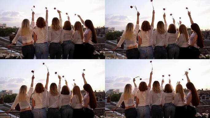 六名诱人的年轻女性从她们的背上连续站在露台上。穿着便服，白衬衫和牛仔裤。用一朵花举起他们的手。前视图