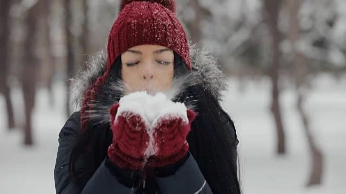 Woman in hat blowing snow to camera at frost winte