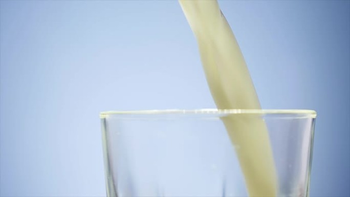 将牛奶倒入玻璃杯中。白色牛奶装满透明玻璃。牛奶倒在白色背景前