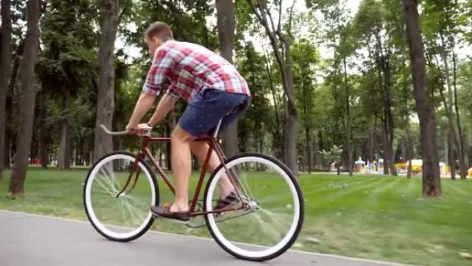 运动男在公园路骑自行车。年轻英俊的男人在户外骑老式自行车。健康积极的生活方式。侧视图特写慢动作低角度