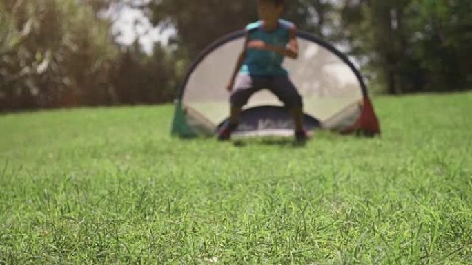 夏令营中快乐的年轻孩子在绿草场踢足球足球比赛儿童踢点球守门员慢动作
