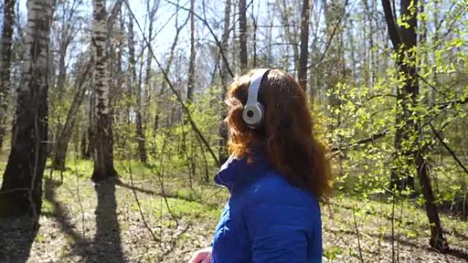 公园里的一个年轻女孩戴着耳机听音乐。一个女人走过春天的公园，欣赏音乐。