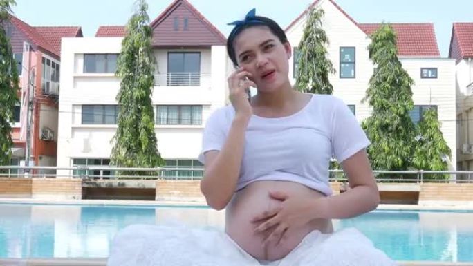 孕妇使用手机，在游泳池边休息