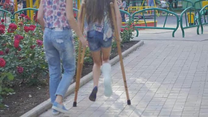 妈妈帮助我拐杖断腿的女儿在街上行走