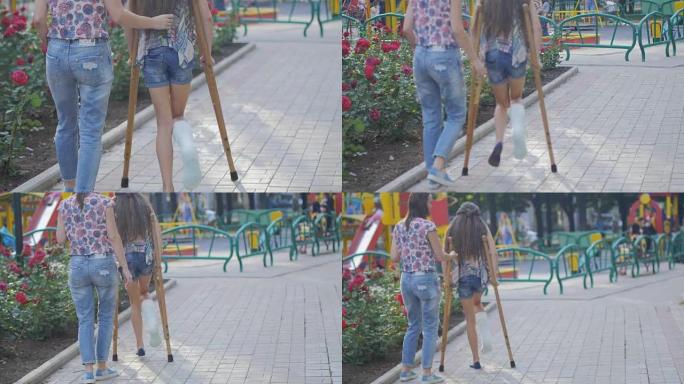 妈妈帮助我拐杖断腿的女儿在街上行走