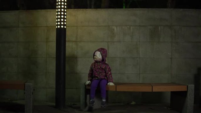 晚上，孩子在公园的灯笼下坐在长凳上。