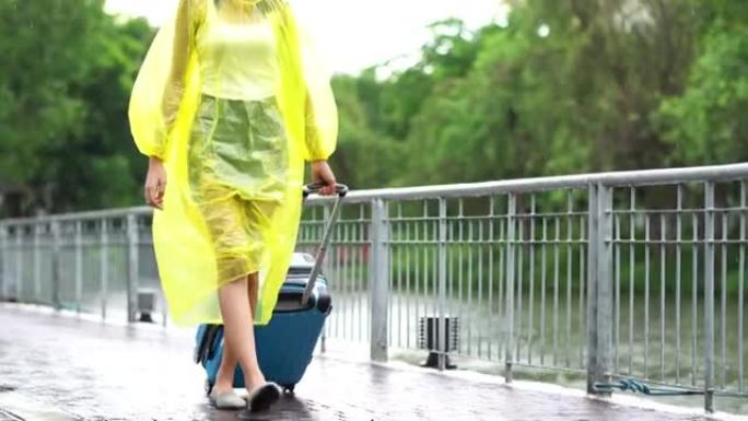 亚洲妇女穿着黄色雨衣在雨中行走，拿着行李箱或行李在公园的街道上行走。