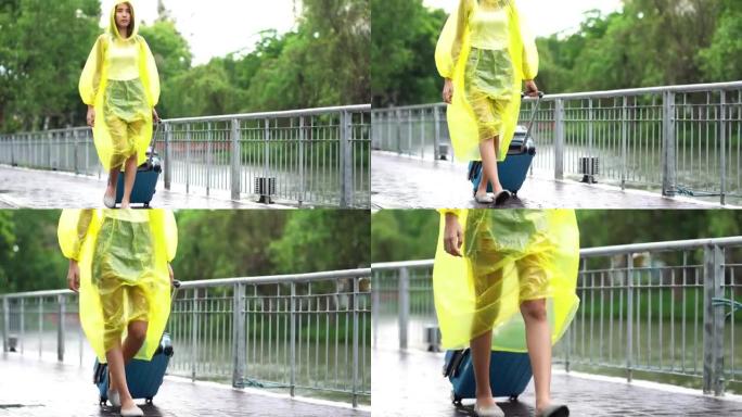 亚洲妇女穿着黄色雨衣在雨中行走，拿着行李箱或行李在公园的街道上行走。