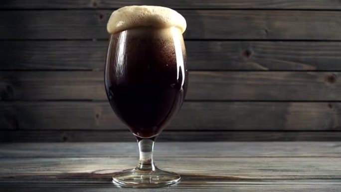 将冷的黑啤酒倒入玻璃杯中。在深色木质背景上。慢动作