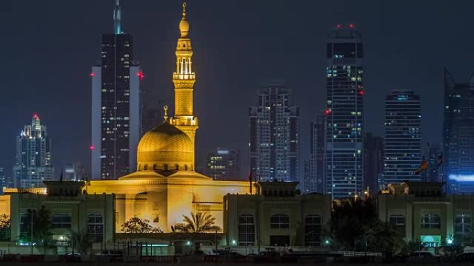 现代迪拜城市天际线与拉希德·哈迪斯清真寺在夜间时光倒流，水面上有照明的摩天大楼