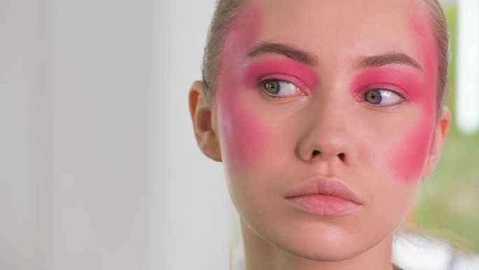 化妆师用化妆刷为年轻金发女人制作美丽的脸部艺术