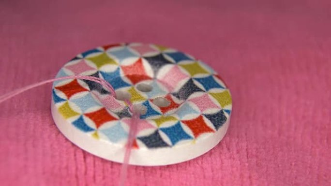 在粉红色的织物上缝制彩色纽扣，用粉红色的线，特写
