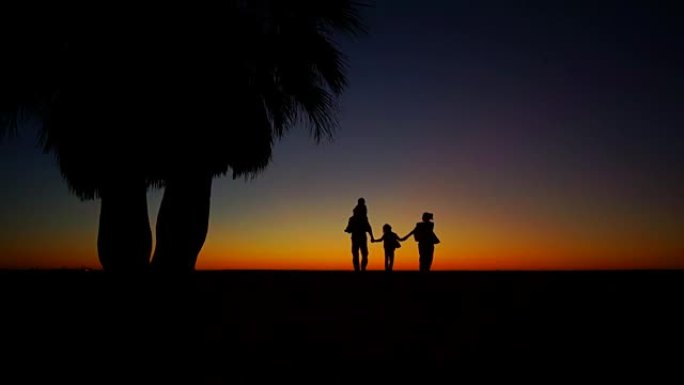 一家人沿着海边散步。成人和两个孩子在海洋日落的背景下度过时光