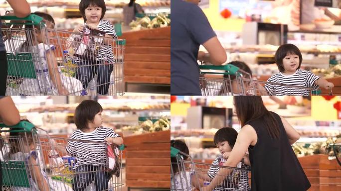 亚洲家庭由购物车上的男孩和女孩组成，父母在杂货店购物