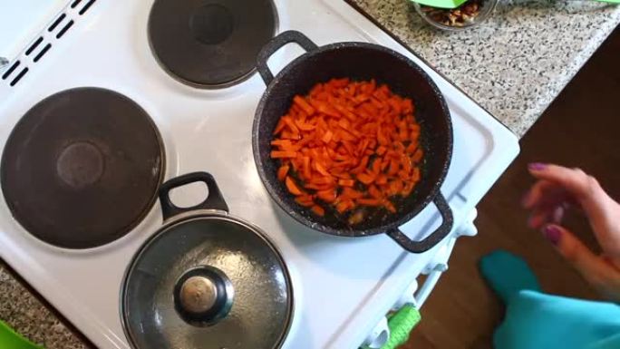 女人把它倒进平底锅里，炸碎胡萝卜。用烹饪刮刀搅拌。