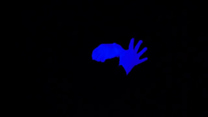 哑剧表演中的紫外线手套。黑色灯光场景中黑色背景上的互动蓝色手。
