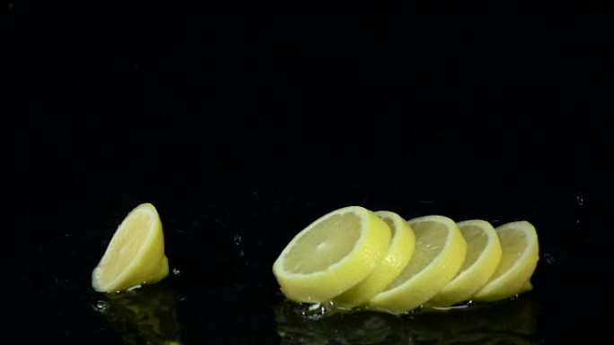 柠檬落入水中时会溶解成薄片。黑色背景。慢动作