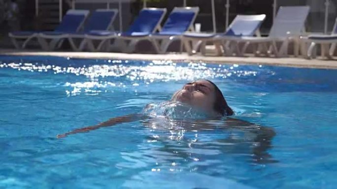 美丽的女孩在游泳池的水下出现。年轻女子从酒店盆地的水底下冒出来。黑发女人在阳光明媚的日子放松。暑假或