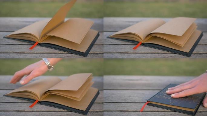 风使躺在长凳上的空白书的书页翻动。街上非常漂亮的设计师笔记本。女性的手合上并拿走了书