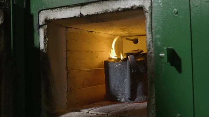 女人铁匠的手从熔化的回收炉烤箱内部检查铝和火焰，然后将其关闭