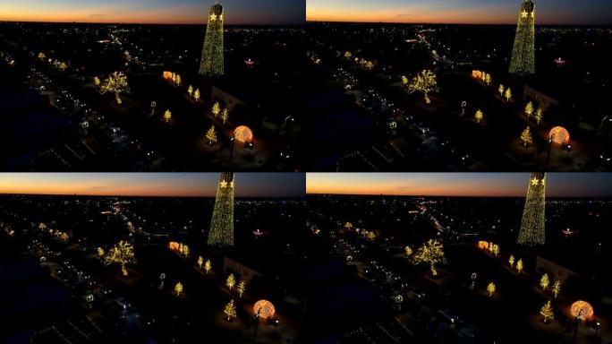 日落后带有水塔的圆形岩石镇广场圣诞节灯光秀的空中无人机视图