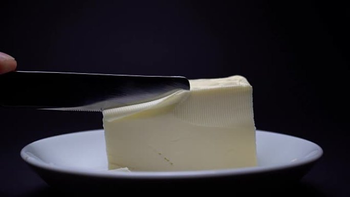 刀切黄油在白色盘子上烹饪，特写，黑色背景。放大。