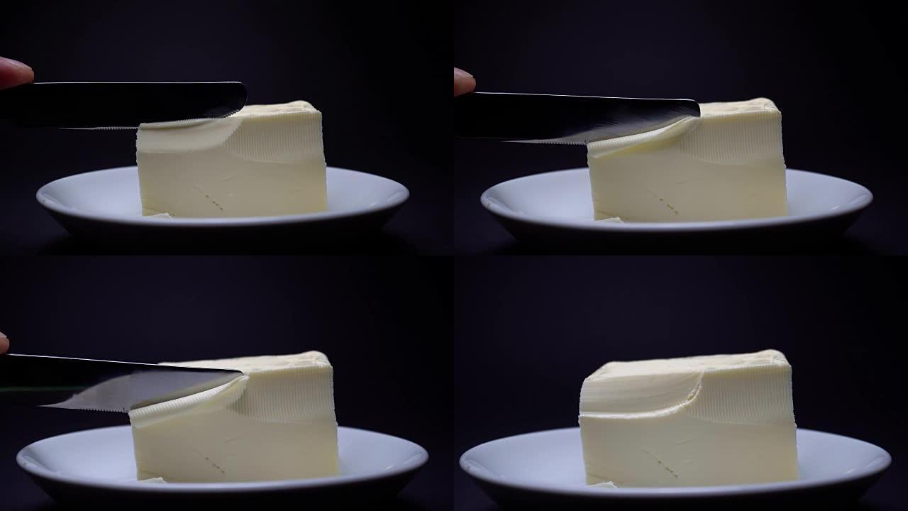 刀切黄油在白色盘子上烹饪，特写，黑色背景。放大。