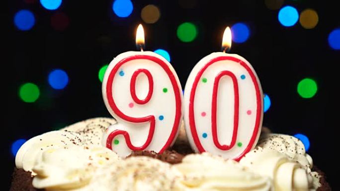 蛋糕上的90号 -- 90岁生日蜡烛燃烧 -- 最后吹灭。彩色模糊背景