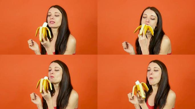 年轻健康的女人，皮肤完美，在明亮的橙色背景下吃香蕉。热带水果。素食概念
