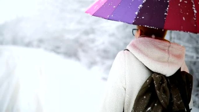 在冬季大自然中散步的年轻女孩拿着彩虹伞