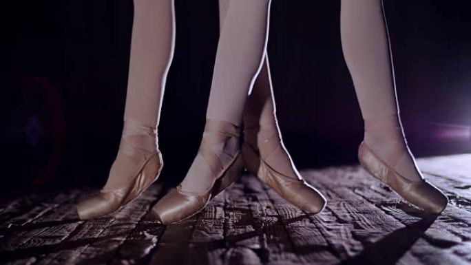 在聚光灯下，在旧剧院大厅的舞台上关闭。芭蕾舞演员穿着脚尖的鞋子抬起脚趾，优雅地进行某种芭蕾舞练习，在