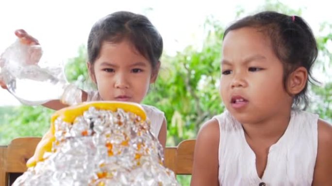 两个亚洲小女孩在家里的桌子上做小苏打和醋火山实验，以100 fps慢动作