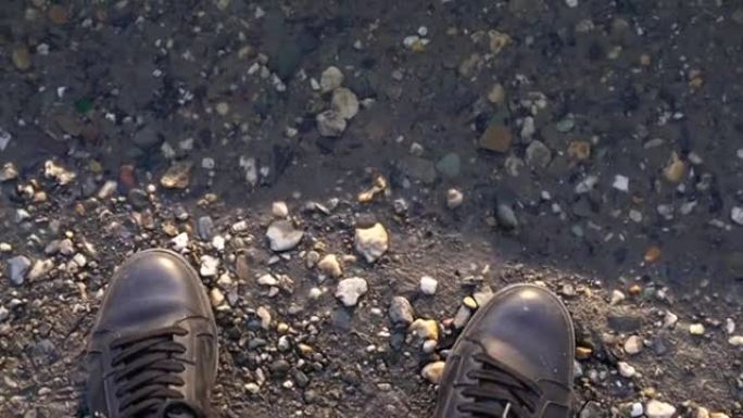 一个穿鞋子的人站在河边或水坑附近，鞋子靠近水