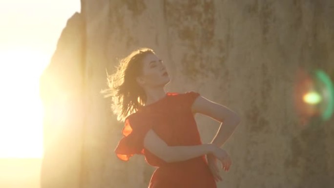 穿着红色连衣裙的女孩在太阳光线和悬崖墙的背景下摆姿势