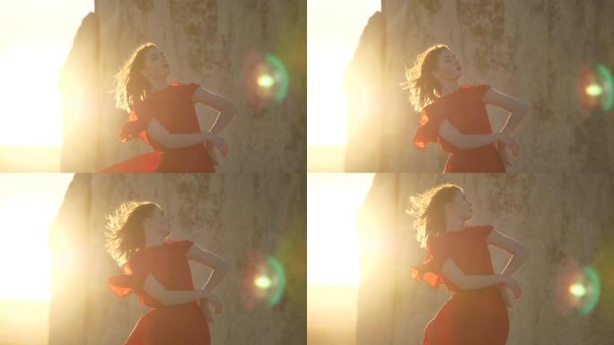 穿着红色连衣裙的女孩在太阳光线和悬崖墙的背景下摆姿势