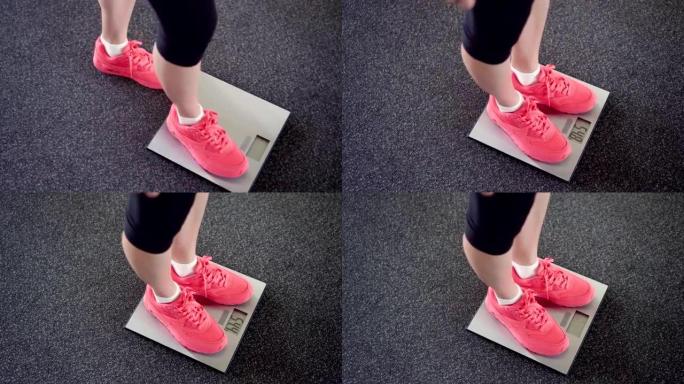 女孩在电子秤上测量她的体重。数字天平上穿着粉色运动鞋的苗条女性腿