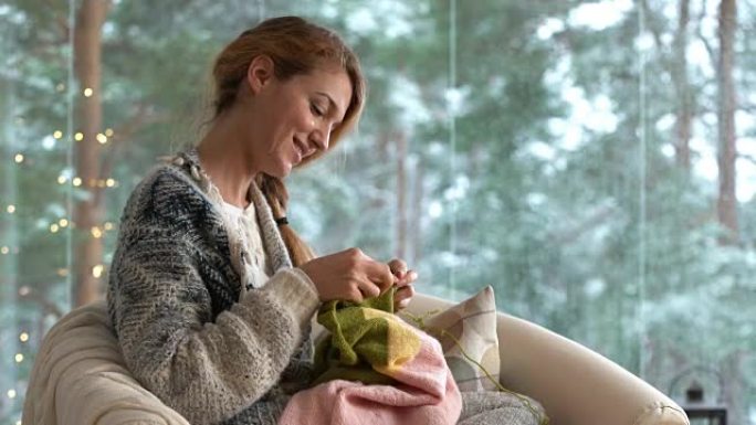 年轻女子在客厅编织保暖羊毛衫，抵御外面的雪景