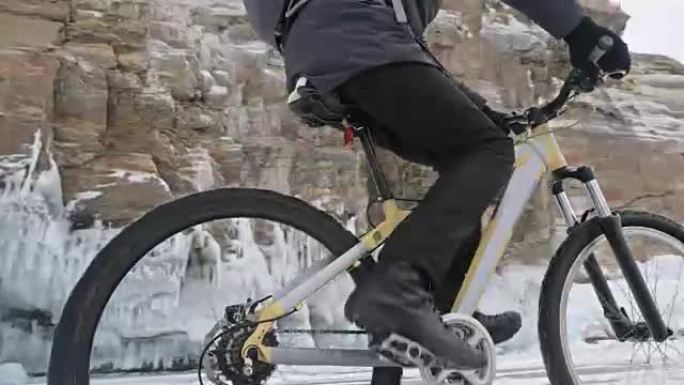 人在冰窟附近骑自行车。有冰洞和冰柱的岩石非常漂亮。骑自行车的人穿着灰色羽绒服，骑自行车的背包和头盔。