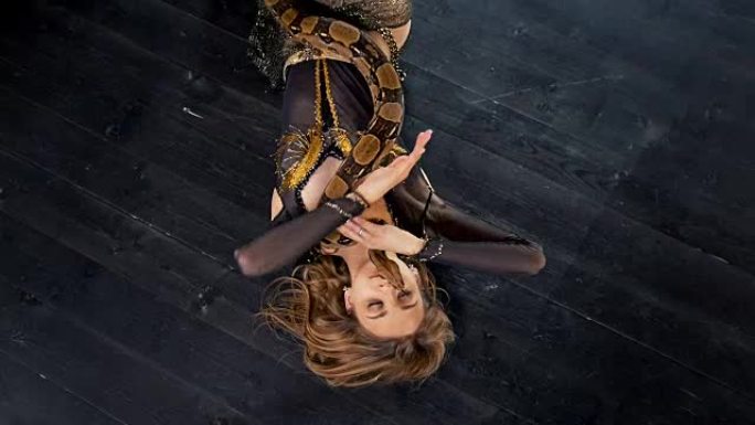 穿着鲜艳服装的迷人女人与蛇躺在地板上跳舞