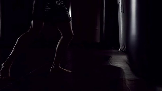 沙袋旁的脚影。慢镜头序列。一个强壮的运动员进入沙袋。在跆拳道里的男人在健身房里训练手提包。慢动作