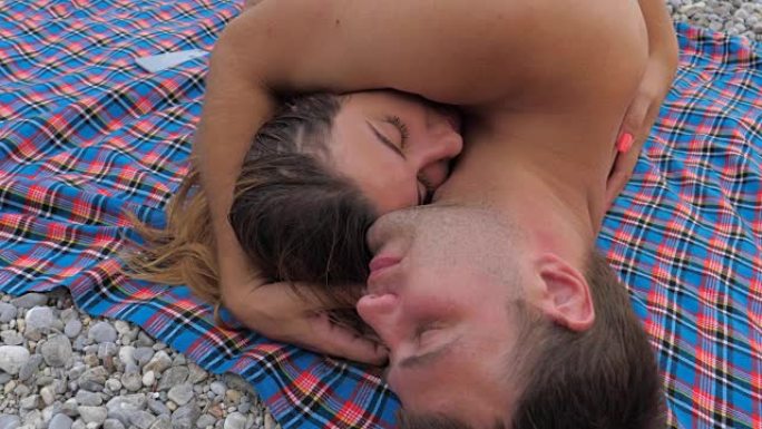 可爱的年轻夫妇穿着泳衣躺在沙滩上拥抱亲吻