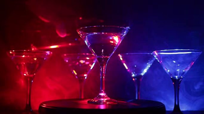 酒精饮料倒入马提尼酒杯中。几杯著名的鸡尾酒马提尼酒，在带有深色雾气背景和迪斯科灯光的酒吧拍摄。俱乐部