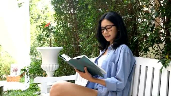 迷人的亚洲女性在花园里微笑着读书。
