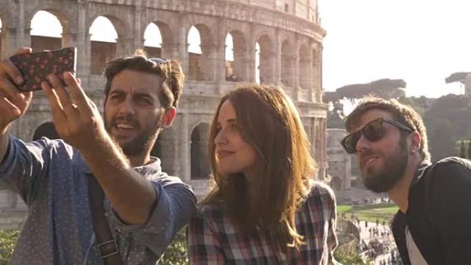 罗马斗兽场的三个快乐的年轻朋友游客在日落时用智能手机棒在山上做鬼脸慢动作steadycam