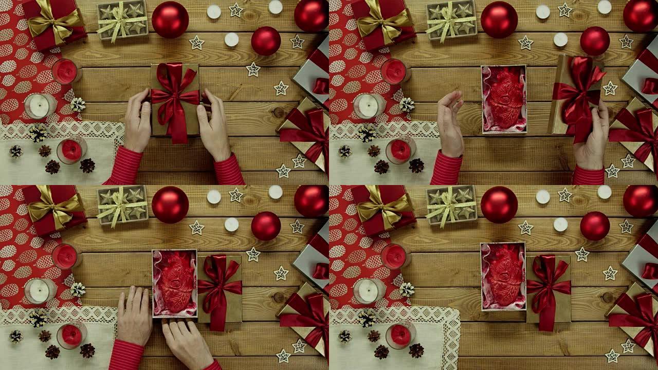 男人在装饰的木桌上用塑料制成的真正的人的心打开圣诞礼物，自上而下拍摄